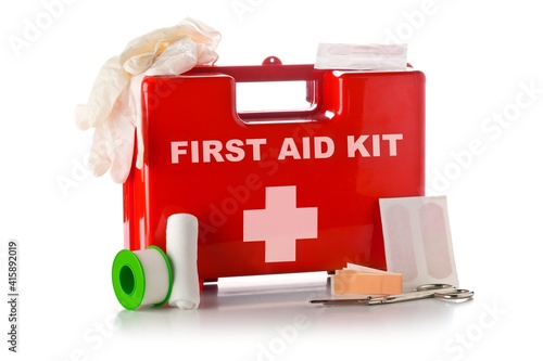 Red first aid medical kit box with scissors, bandage, tape and gloves standing over white