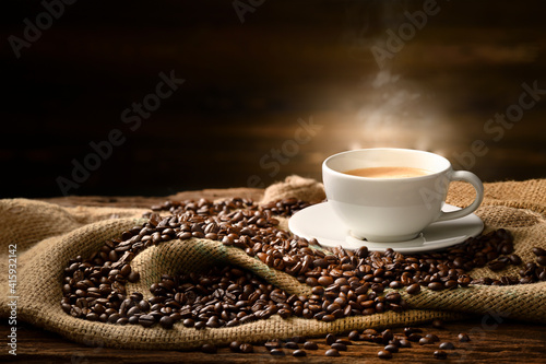 Cup of coffee with smoke and coffee beans on burlap sack on old wooden background