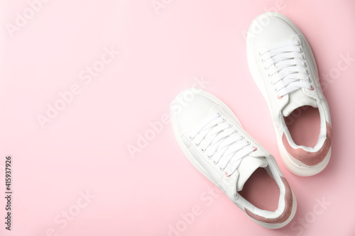 Stylish white sneakers on pink background, top view. Space for text