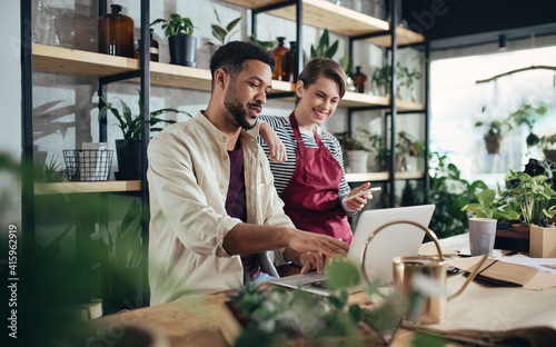 Shop assistants with laptop working in potted plant store, small business concept.