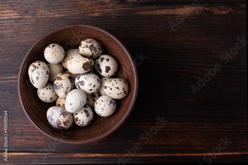 Fresh quail eggs in a bowl on a dark wooden background, rustic style.