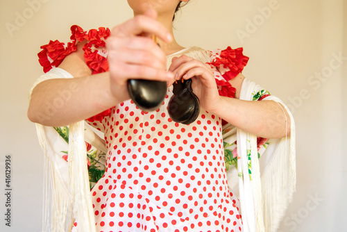 Detalle de una mujer española vestida con un vestido de lunares rojos de flamenca y un mantón de manila blanco tocando las castañuelas. Concepto de bailarina de sevillanas. Flamenco.