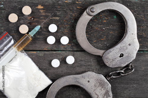 Syringe with cocaine and police handcuffs on a dark wooden background, top view