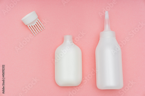 a white tube with paint and a bottle with a convenient applicator for the developing emulsion for self-dyeing hair at home on a pink background. saving time and money. home beauty salon.