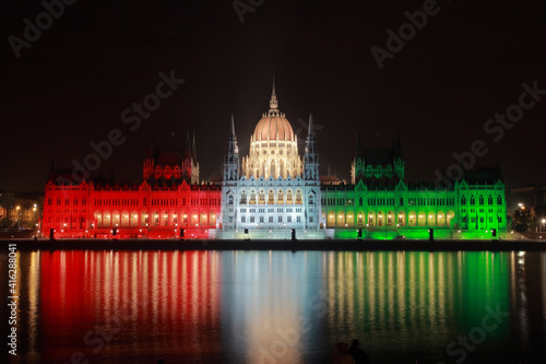 The hungarian Parliament by night lit in national colors red, white and green on the Danube bank; color photo.