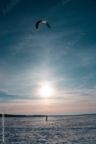 Vertical outdoor action photography with a single extreme ski kiter, riding with parachute due to strong wind against bright winter sun shining in the blue sky