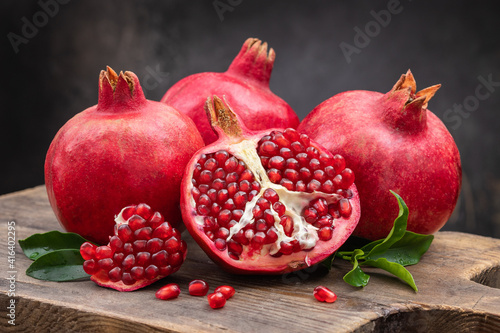 Healthy pomegranate fruit with leaves and open pomegranate on an old wooden board, side view, dark vintage background.