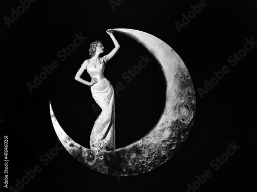 Young woman in evening elegant dress. Fashion Night dress. Beautiful young women posing on crescent moon on black background. Girls dream.