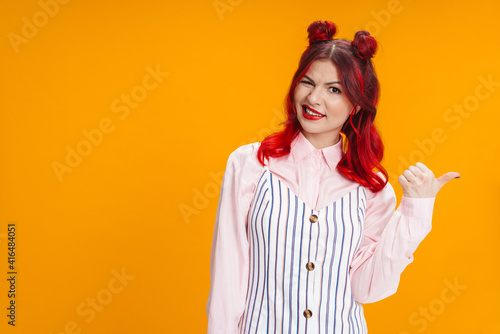 Beautiful girl with red hair winking while pointing finger aside