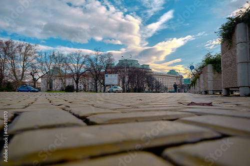 Center of Sofia Bulgaria. Photo taken from low angle of yellow cobblestones with cars and sun rising sky background. Bulgaria. Sofia. 06.01.2021