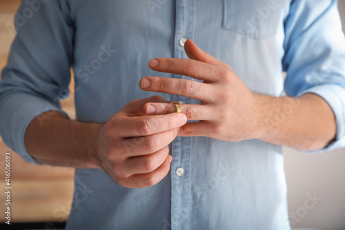 Man taking off wedding ring on blurred background, closeup. Divorce concept