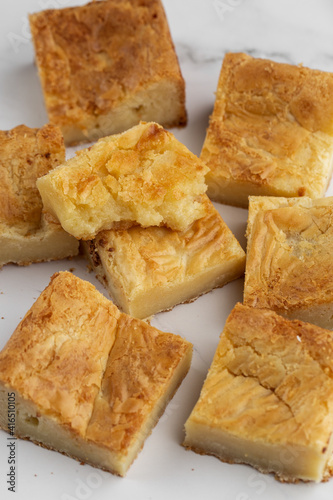 Pieces of freshly baked white chocolate brownies in square form. Flat lay composition with sweet white brownies isolated on white marble background. Delicious blondie brownies. Dessert menu concept.