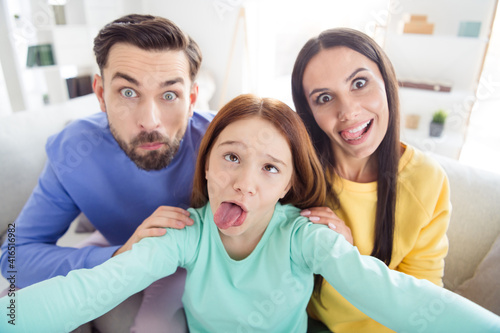 Photo of cheerful family mommy daddy daughter happy positive smile have fun grimace fooling tongue-out make selfie home