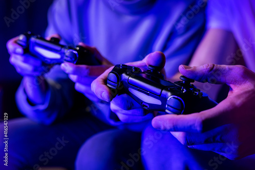 friends playing console video games. controller in hands closeup. neon lights