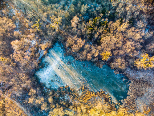 Aerial drone winter scenery on frozen wintery small wild lake in forest in warm sunset light. Fly above natural park aerial view 90 degrees