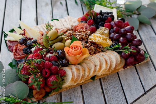 Elegant charcuterie grazing board filled with assorted meats , cheeses, fruits, nuts, olives, and garnishes 