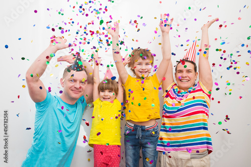 happy family mom, dad and two kids brother and sister with confetti on colored 
