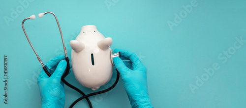 Health care cost. Doctor in surgical gloves holding a white piggy bank and stethoscope