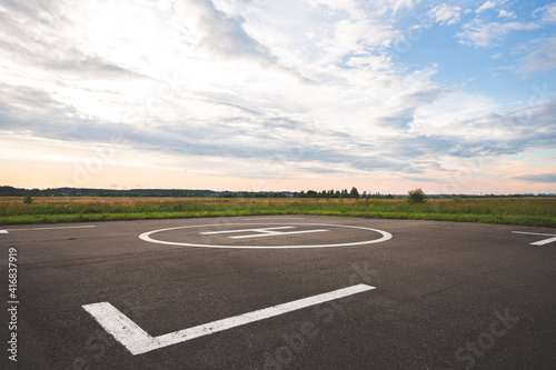 A large area with a special symbol in the center for helicopter landing. Private helipad in a green field against the backdrop of evening clouds.