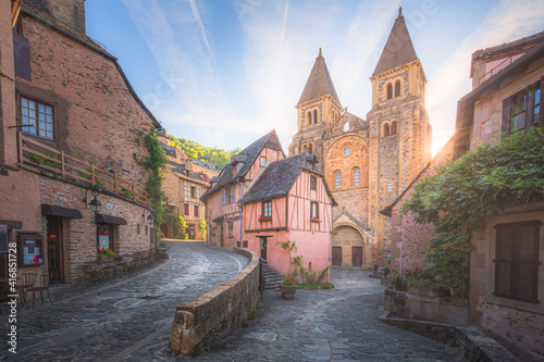 The quaint and charming town centre of the medieval French village Conques, Aveyron and Abbey Church of Sainte-Foy at sunset or sunrise in Occitanie, France.