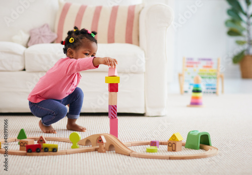 cute african american toddler baby girl playing wooden toys, stacking the tower blocks on the carpet at home