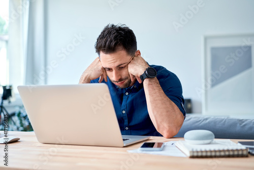 discouraged young man looking with disappointment on laptop while working at home