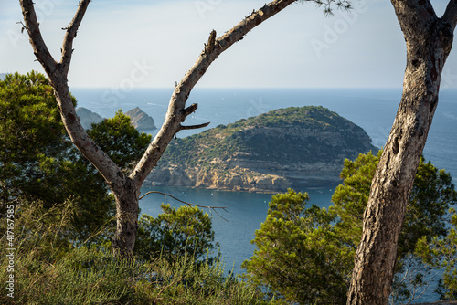 View of the island of Portichol in the calm turquoise waters of the Mediterranean Sea from Cap Negre viewpoint on a day with blue sky, Javea , Alicante, Spain