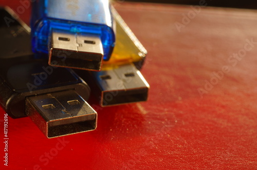 USB flash drive - black, yellow and blue, on a red background. Three used computer flash drives, ready to work. Close-up of a data memory stick, in several colors, on a bright background.