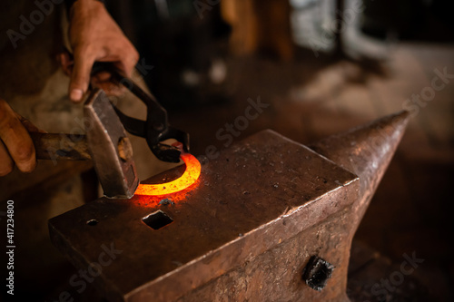 The blacksmith forging the molten metal on anvil in smithy. Blacksmith at the workshop. Working metal with hammer and tools in forge