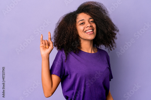 Young african american curly woman isolated on purple background showing a horns gesture as a revolution concept.
