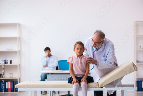 Small girl with her father visiting old male doctor