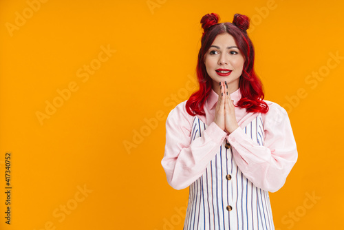 Pleased girl with red hair posing and holding palms together