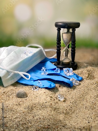 A mask and protective gloves are lying on the sand, the hourglass is counting down 