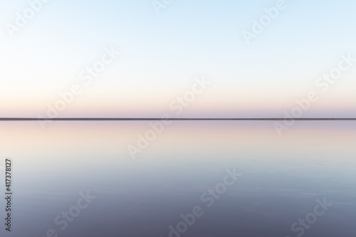 Tranquil minimalist landscape with smooth surface of the pink salt lake with calm water with horizon with clear sky in sunrise time. Simple beautiful natural calm background