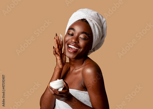 Beautiful young african american woman applying cream on face