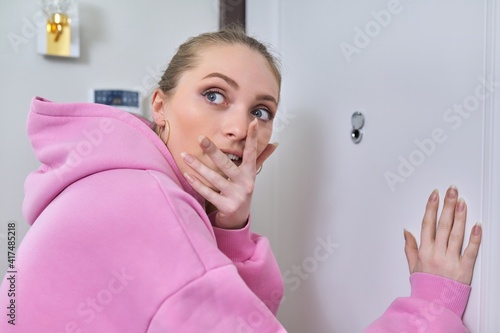 Young woman looking through peephole of front door in apartment.