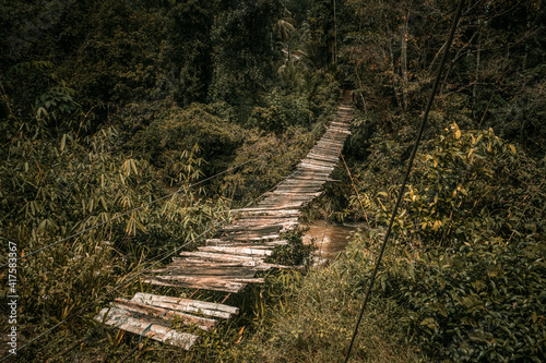 Drewniany most linowy rozwieszony pośród dżungli.