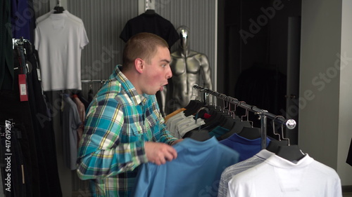 A young man chooses a shirt in a store and is surprised at the expensive price of a shirt. Clothing store.
