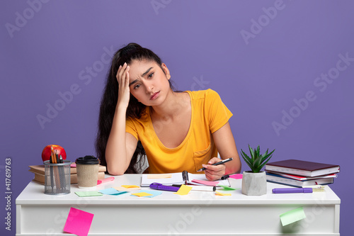 Tired indian woman sitting at desk writing