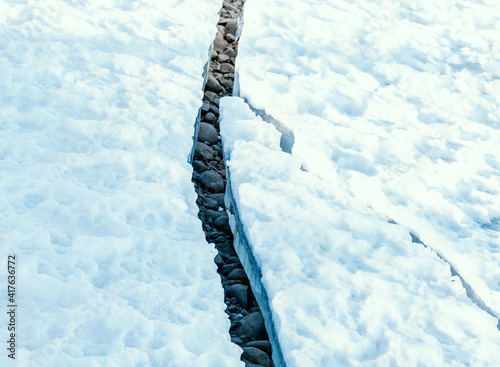 Large crack in permafrost ice revealing dry rocks hidden beneath.