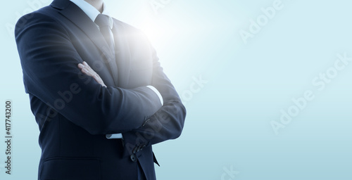 Confident business manager with crossed arms. Pale blue background with backlit.