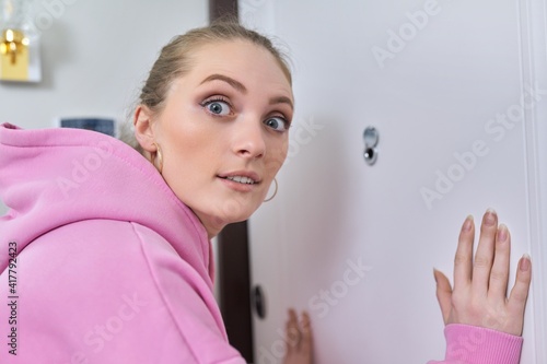 Young woman looking through peephole of front door in apartment.