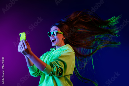 Photo of amazed shocked young woman look phone fast internet fly hair isolated on colorful neon background