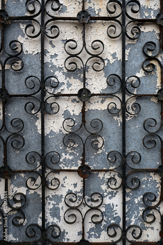 Wrought iron fence or gate on a weathered blue wall with cracked white paint. Portrait orientation.