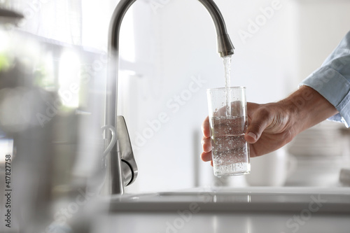 Man pouring water into glass in kitchen, closeup