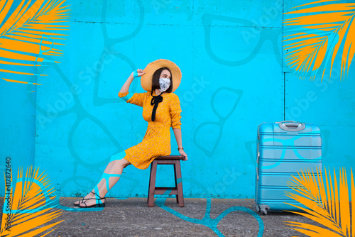 Woman in a yellow dress sitting in front of a blue background with her luggage by her side