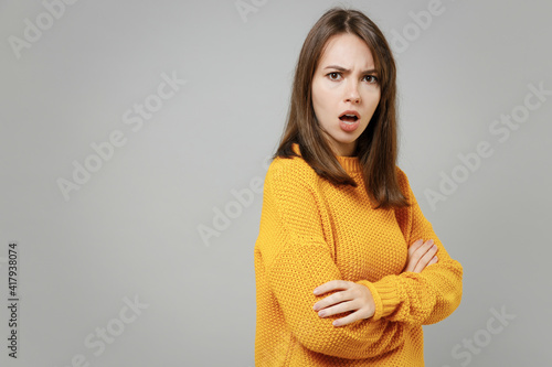 Young excited happy cute indignant confused caucasian woman 20s wearing casual knitted yellow sweater holding hands crossed folded looking camera isolated on grey color background studio portrait.