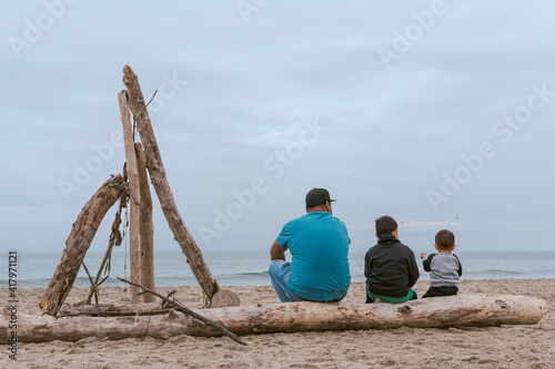 Familia Mexicana compuesta por un padre y sus dos hijos sentados sobre un tronco en una playa de Santa Cruz, California, Estados Unidos.