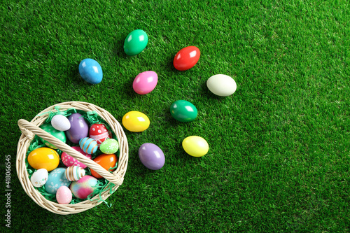 Wicker basket with Easter eggs on green grass, flat lay. Space for text