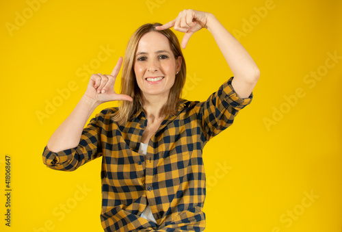 Happy woman making frame with fingers isolated over yellow background